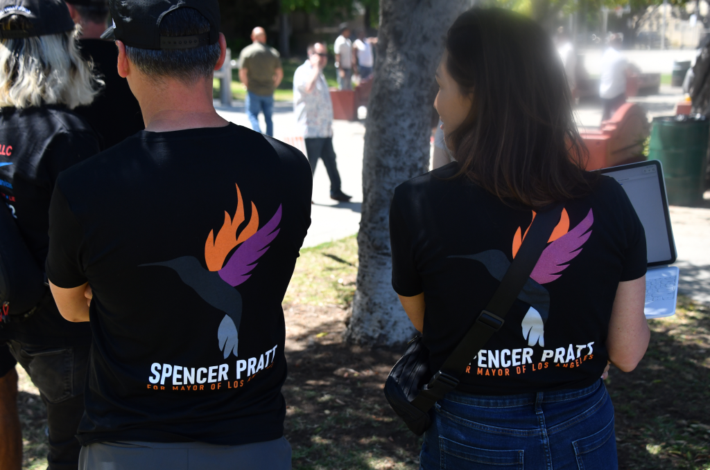 The back of two people wearing black t-shirts with a hummingbird design and the words "SPENCER PRATT FOR MAYOR OF LOS ANGELES" printed on them.