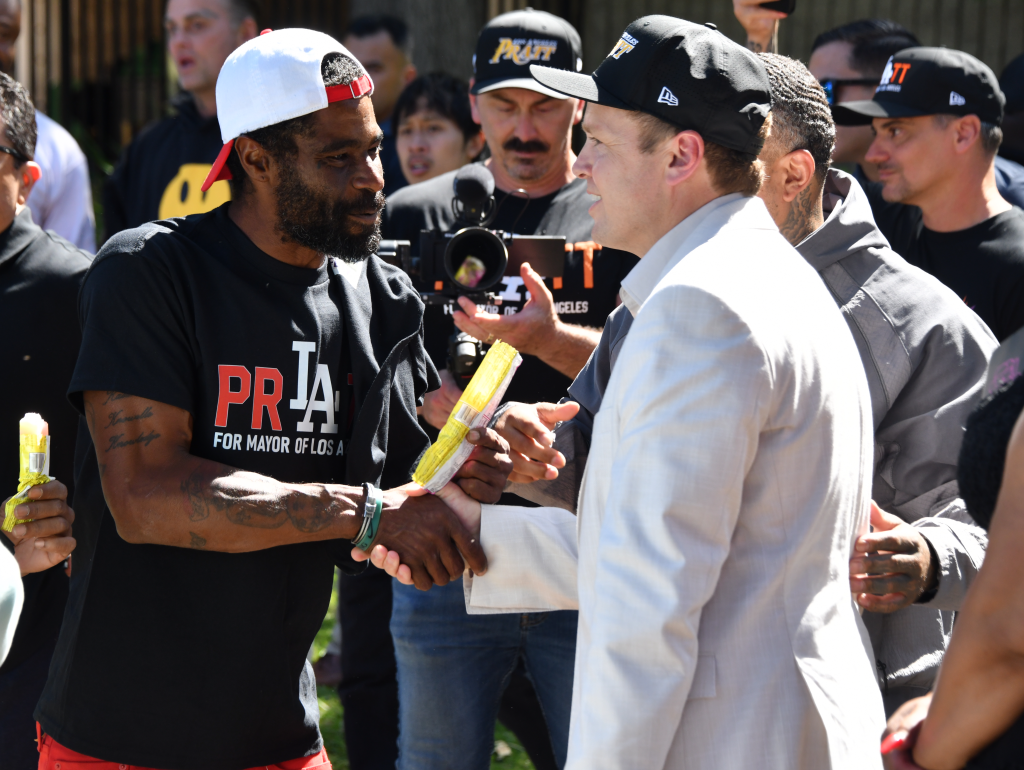 Spencer Pratt shaking hands with an African American man wearing a "Pratt for Mayor of Los Angeles" t-shirt, at a political event.