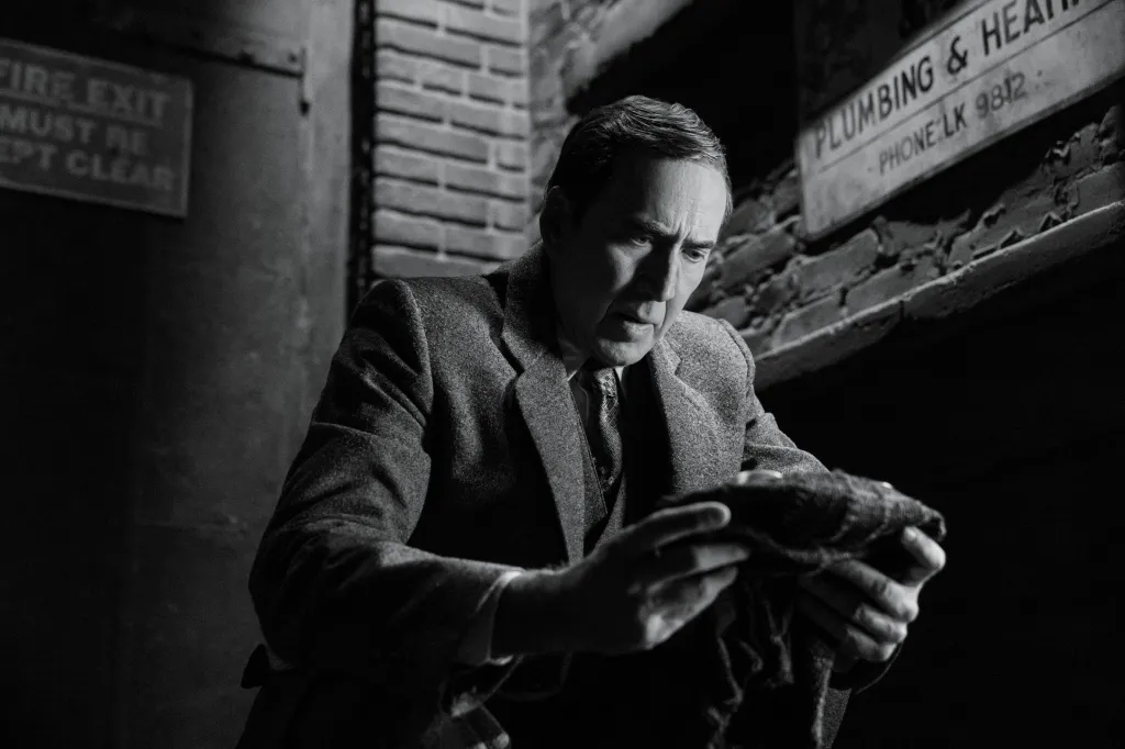 Nicolas Cage as Spider-Noir, looking down intently while holding an object.