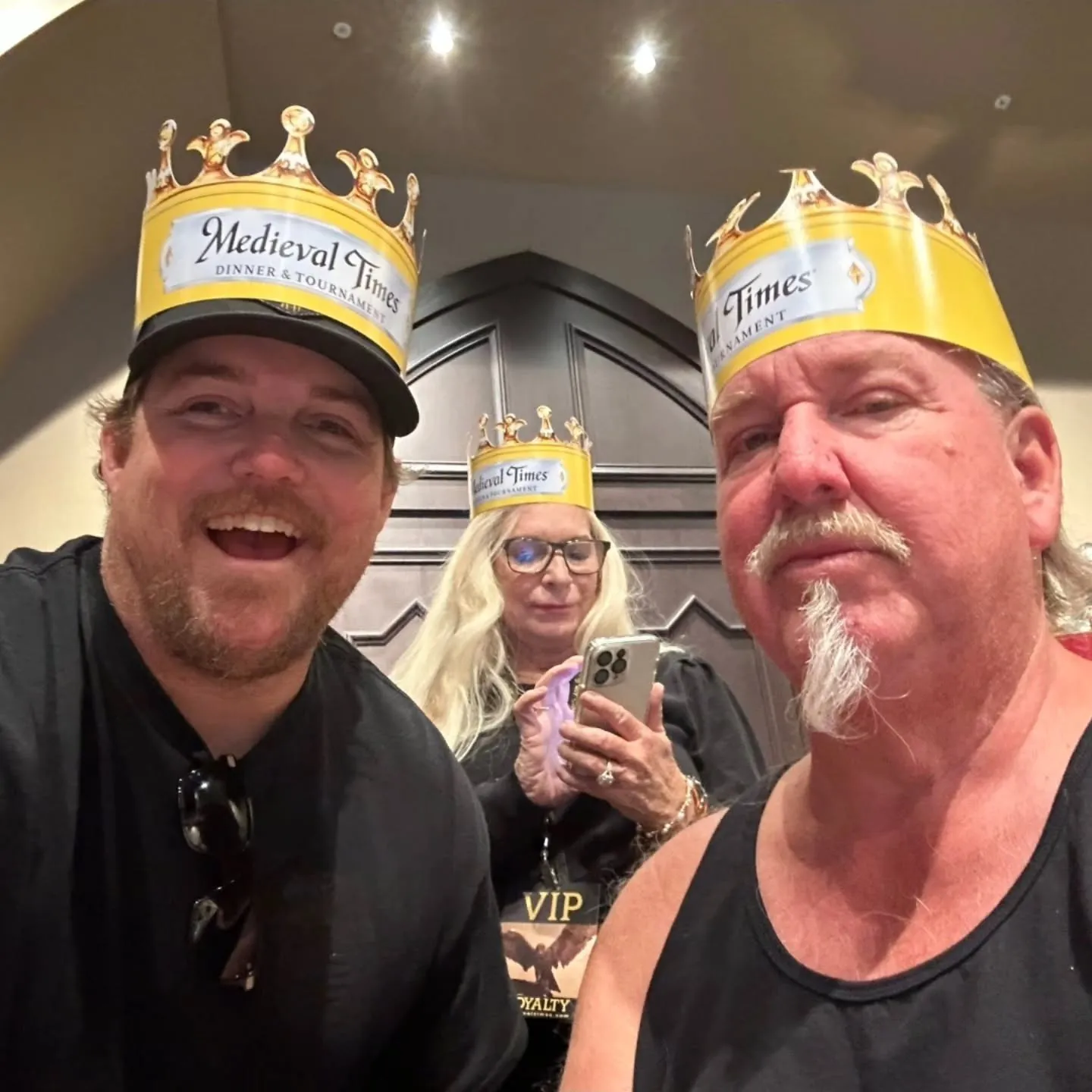 Brandon and Darrell Sheets from "Storage Wars" wearing Medieval Times crowns with a woman holding a phone in the background.