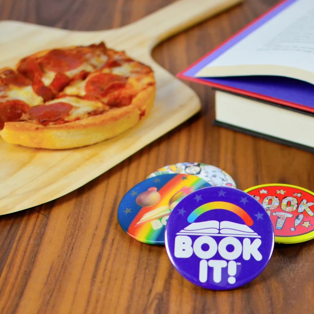 A personal pan pepperoni pizza on a wooden peel next to an open book and three "BOOK IT!" buttons.