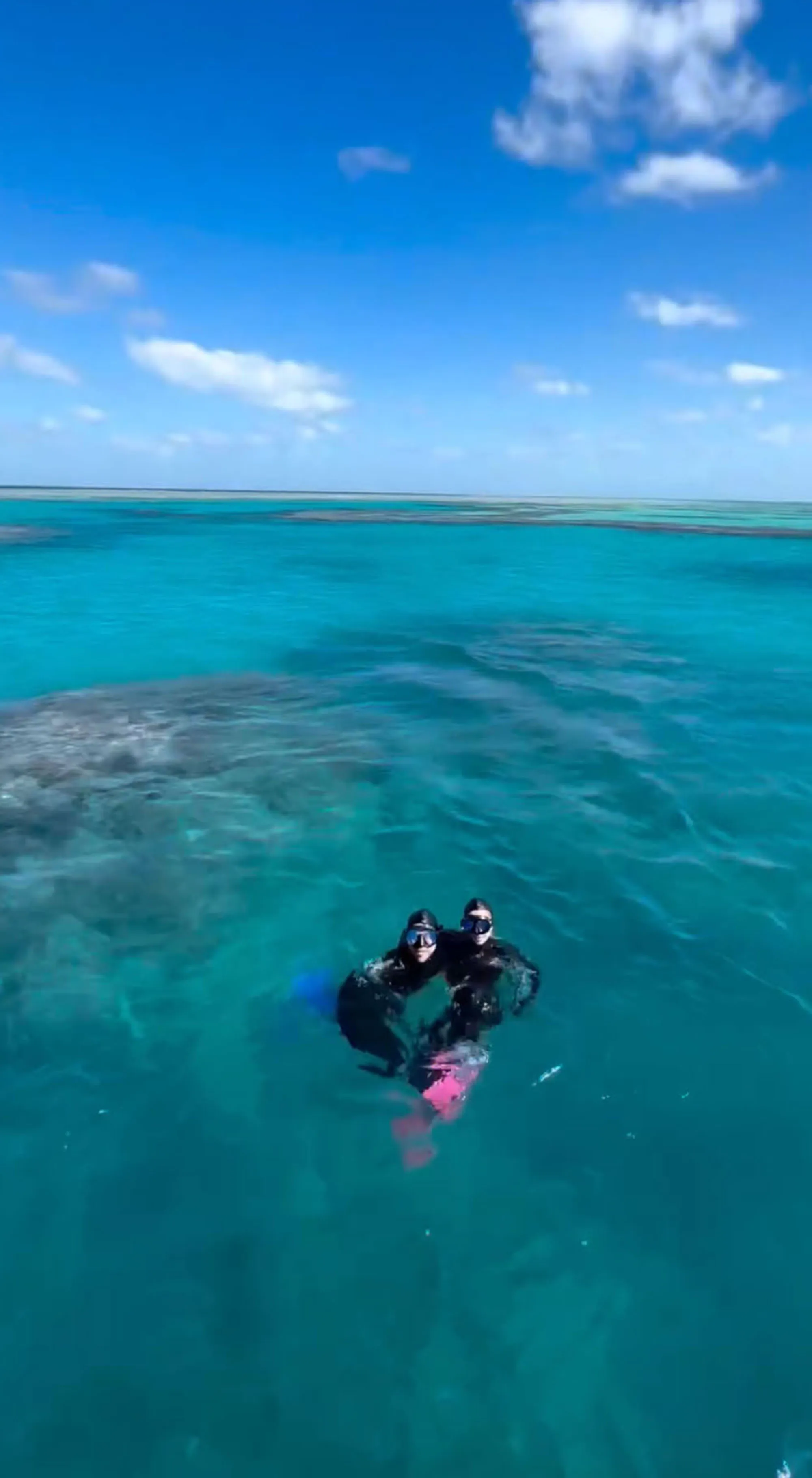 Two people wearing diving masks and snorkels swimming in turquoise water.