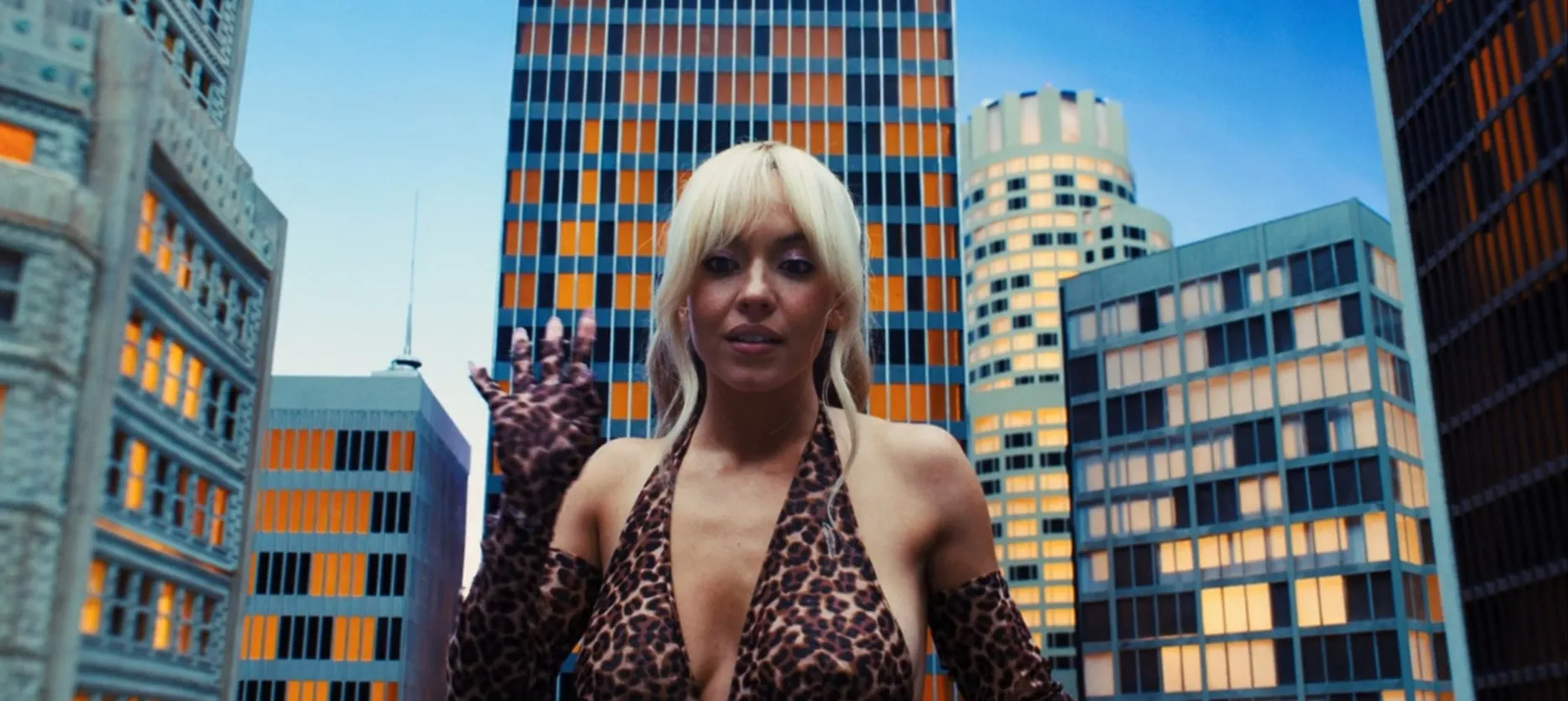 Sydney Sweeney in a leopard print dress, with tall buildings in the background.