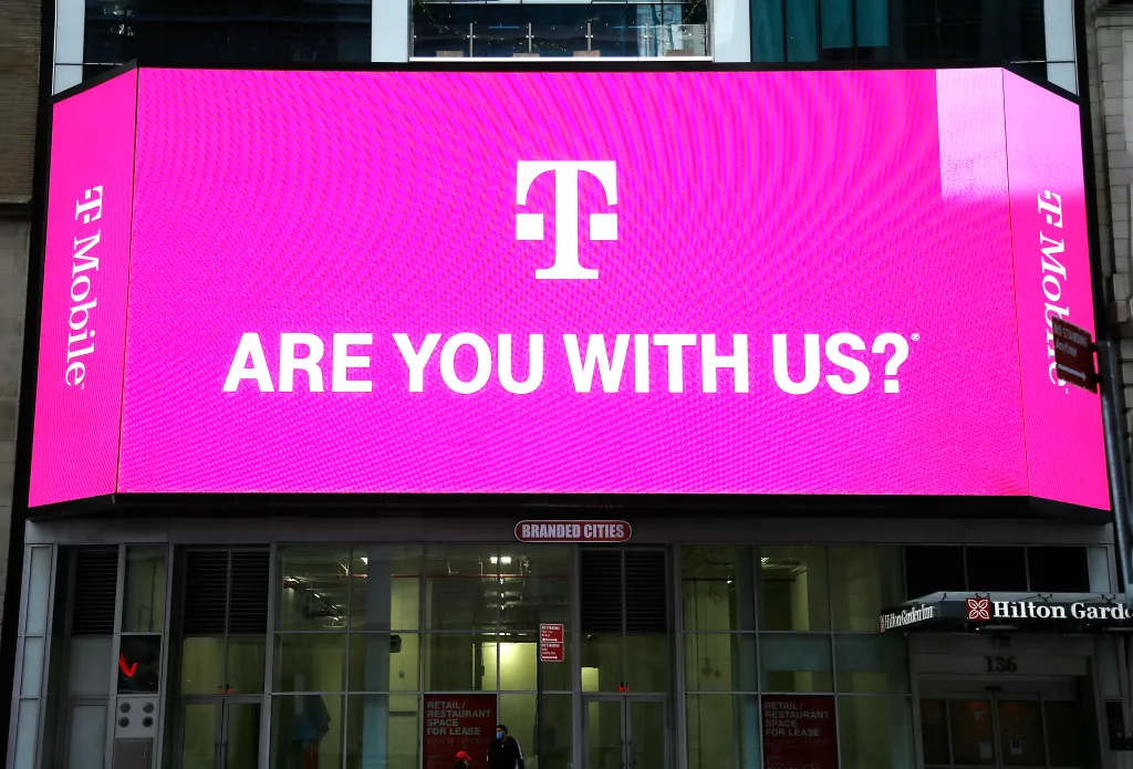 A T-Mobile advertisement on a large digital billboard in Times Square displaying "ARE YOU WITH US?"