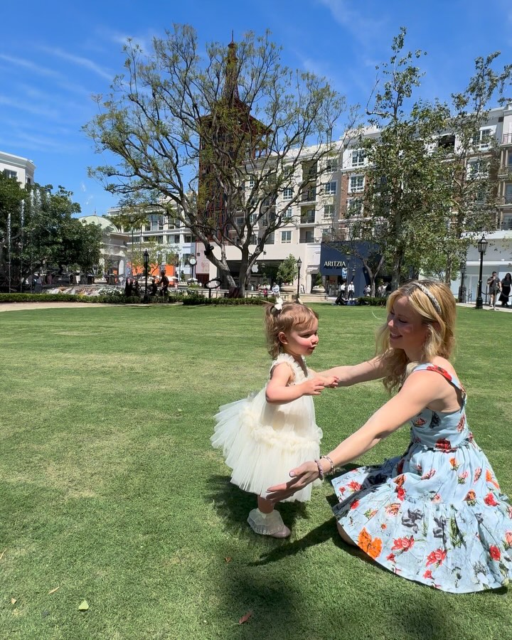 Tara Lipinski playing with her daughter on a grassy area in an urban setting.