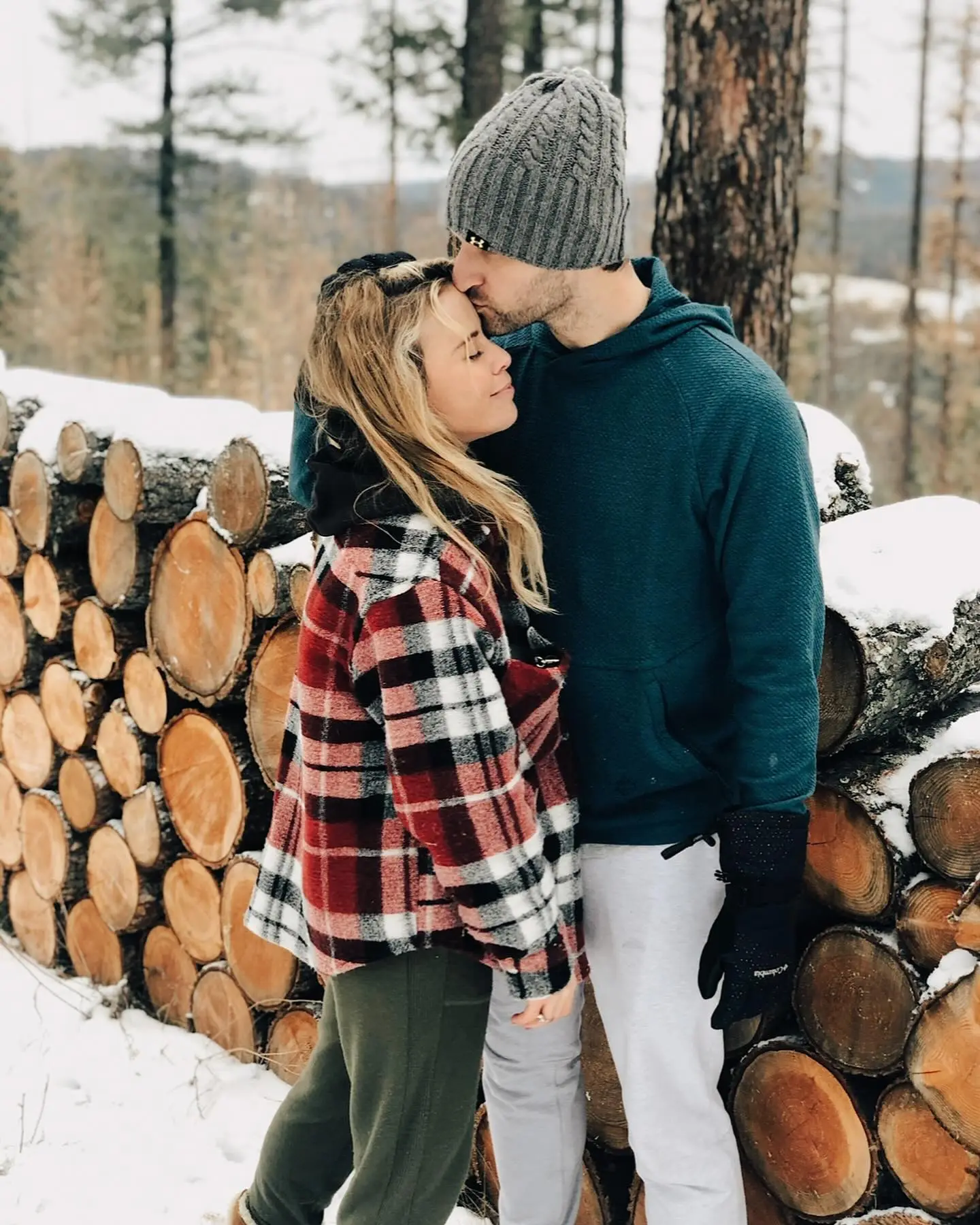 Tara Lipinski and husband Todd Kapostasy embrace in a snowy, wooded area.