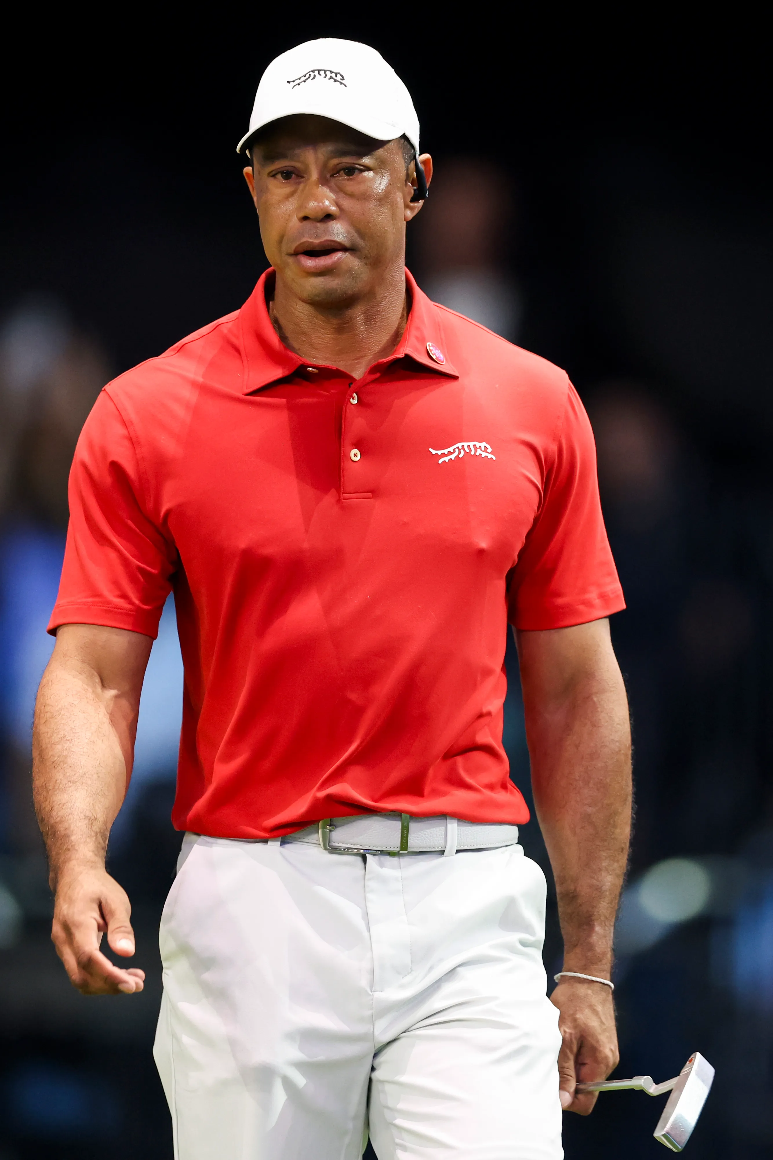 Tiger Woods in a red shirt and white hat, holding a golf club.