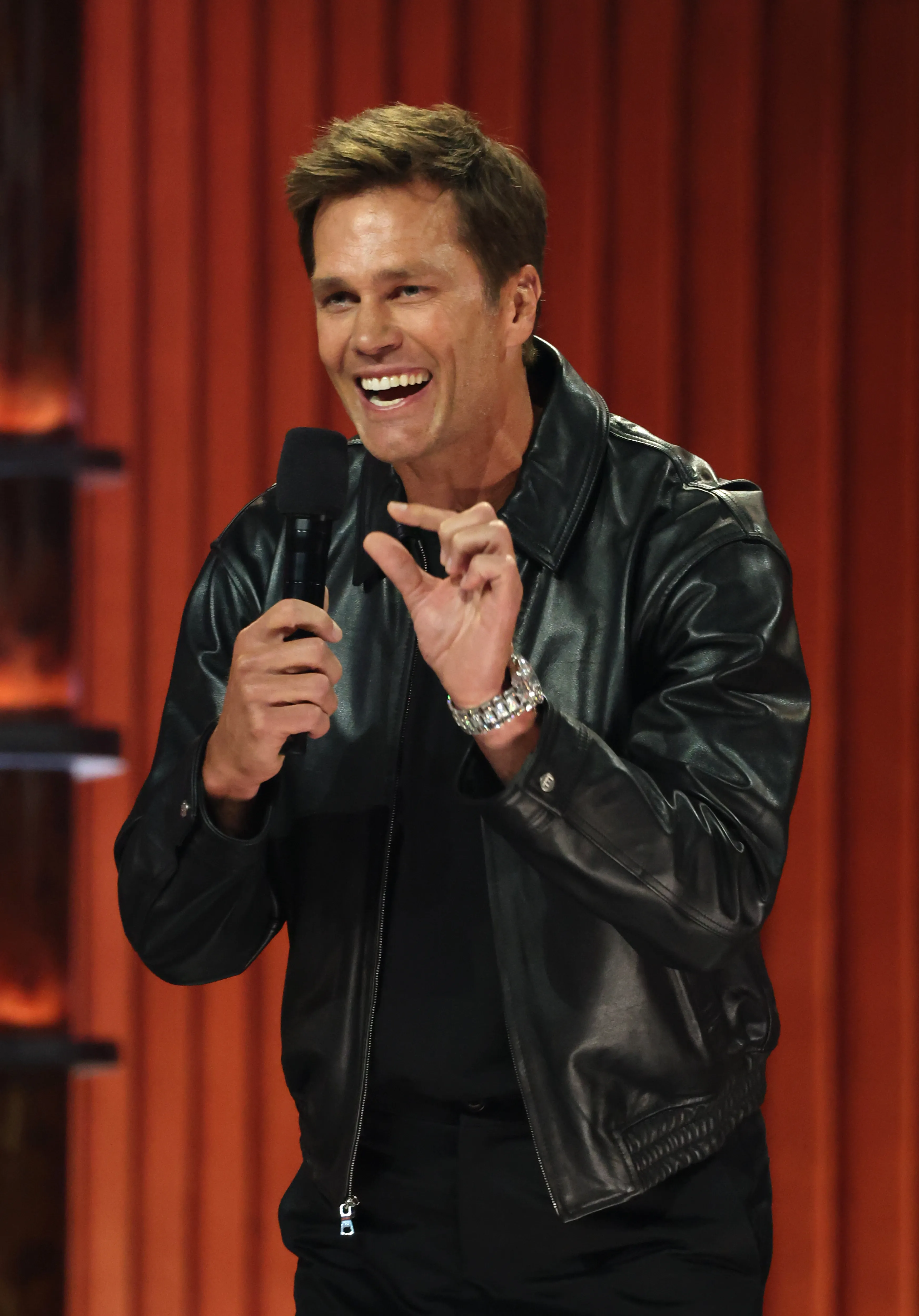 Tom Brady speaking into a microphone on stage.