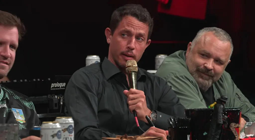 Tony Hinchcliffe holding a gold microphone while looking to the side.