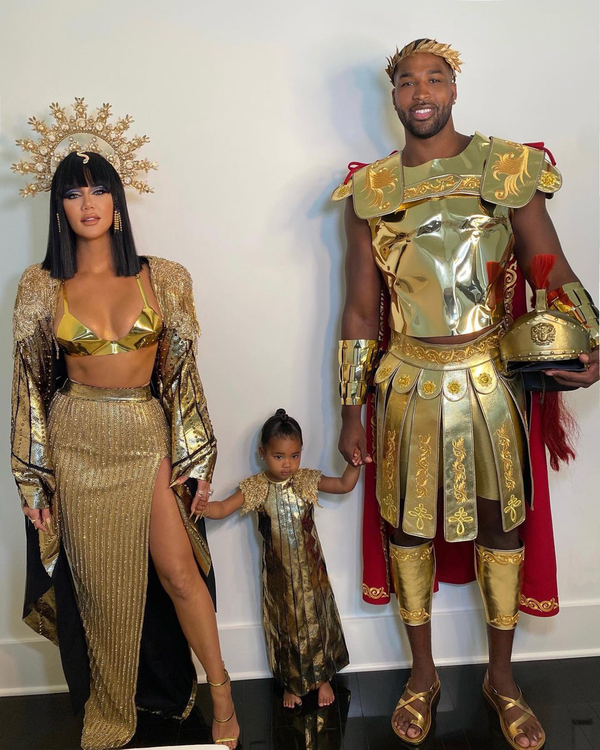 Khloé Kardashian, Tristan Thompson, and their daughter dressed in gold costumes.