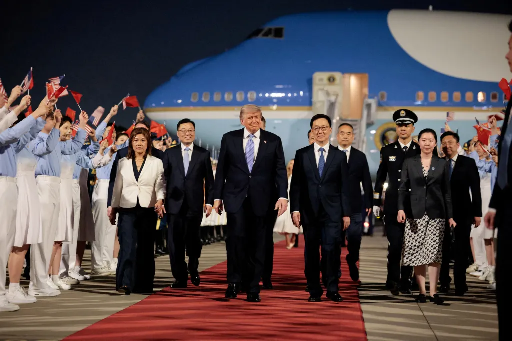 Donald Trump walks with Chinese Vice President Han Zheng on a red carpet at Beijing Capital International Airport, with people holding US and Chinese flags in the background.