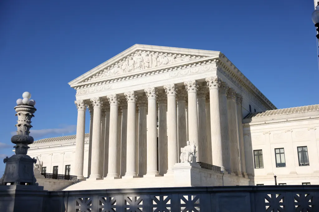 The United States Supreme Court Building in Washington, D.C., with its classical facade and columns, under a blue sky.