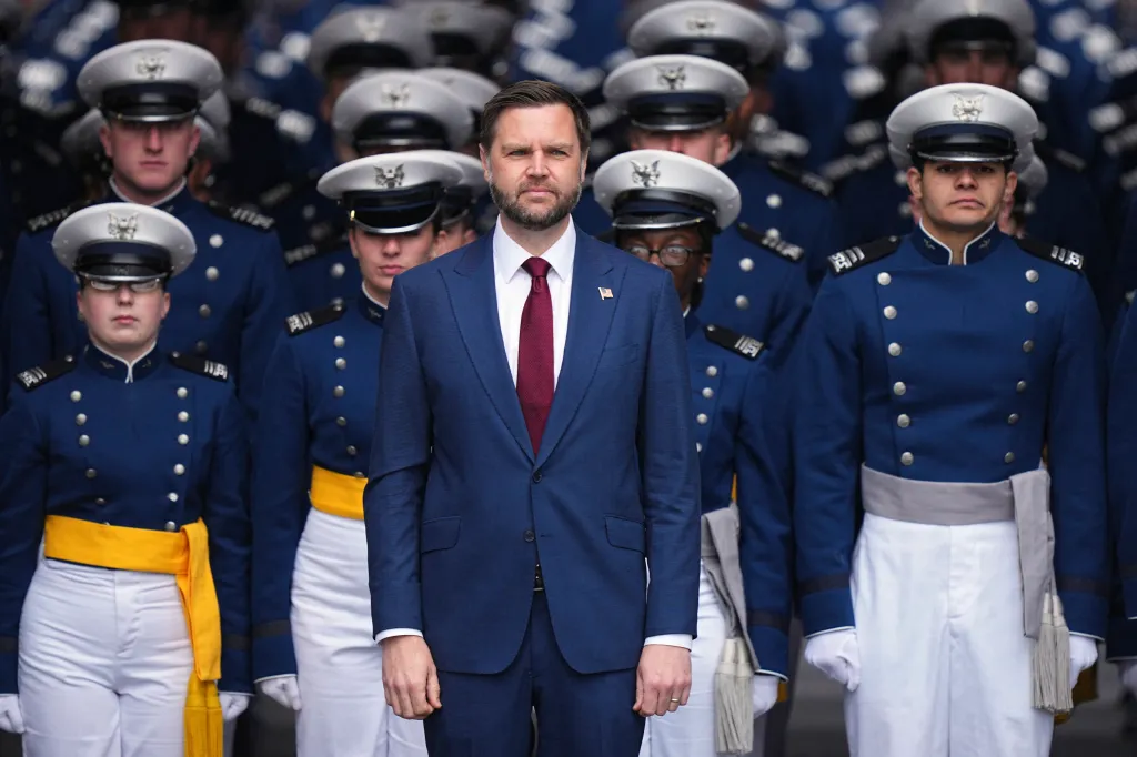 Vice President JD Vance in a blue suit and red tie, standing amidst Air Force Academy cadets in their dress uniforms.