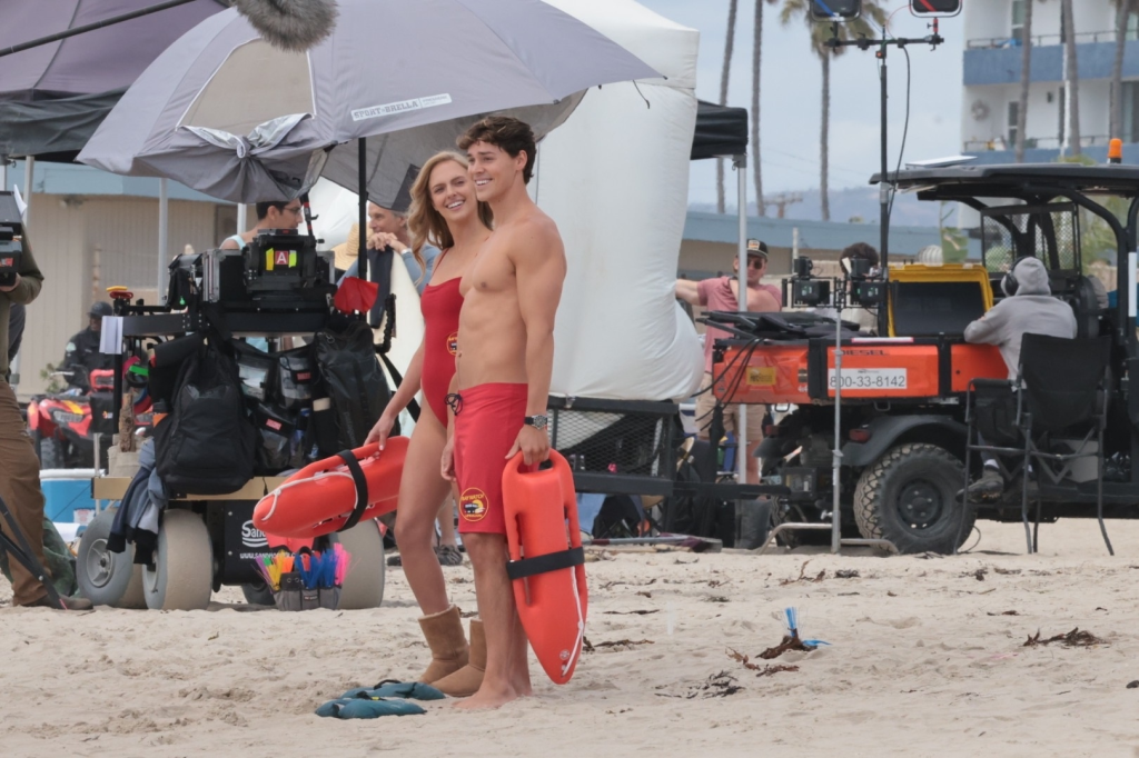 Noah Beck and Jessica Belkin dressed as lifeguards, holding rescue buoys while filming "Baywatch" in Venice Beach.
