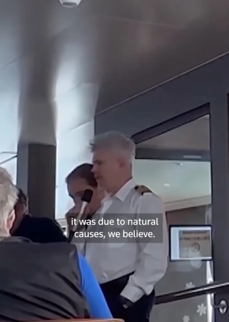 Video still of a cruise ship captain in uniform speaking into a microphone with text overlay: "it was due to natural causes, we believe."