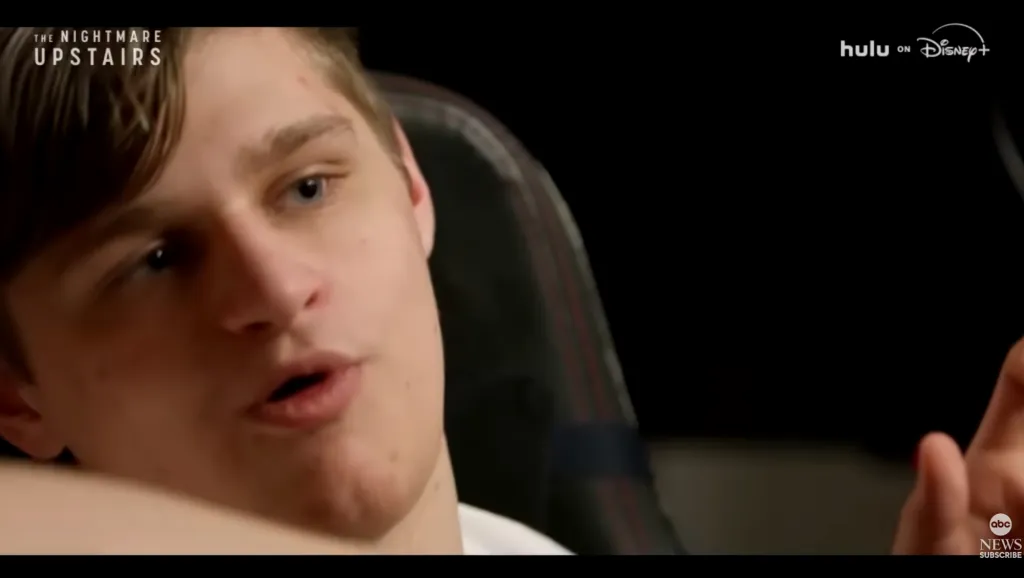 A young man with light hair and blue eyes, Brynlee Larson, speaking to the camera in "The Nightmare Upstairs" documentary.