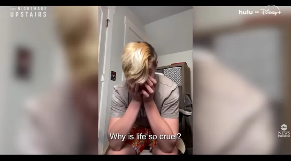 A young person with bleached blonde hair sitting down, covering their face with their hands, with the text "Why is life so cruel?" superimposed on the image.