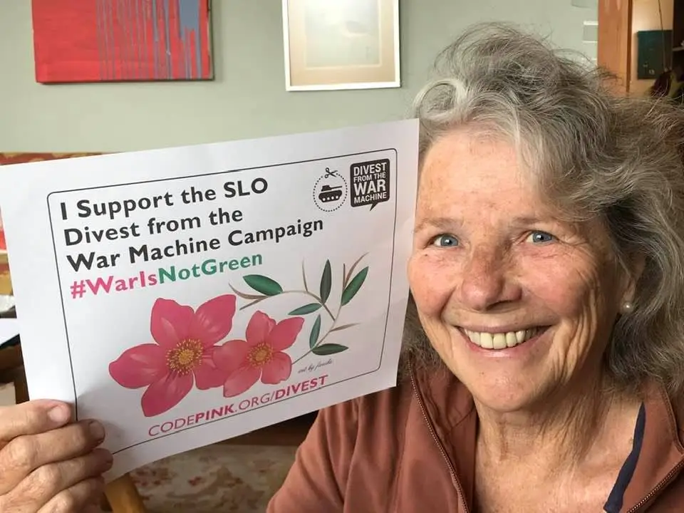 Linda Seeley holding a sign that reads, "I Support the SLO Divest from the War Machine Campaign #WarIsNotGreen".