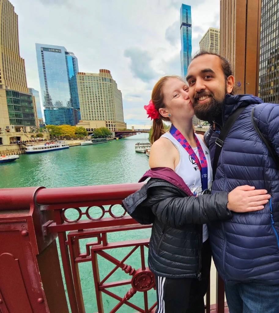 Catie and Josh from 90 Day Fiance pose for a photo on a bridge, with Catie kissing Josh's cheek.
