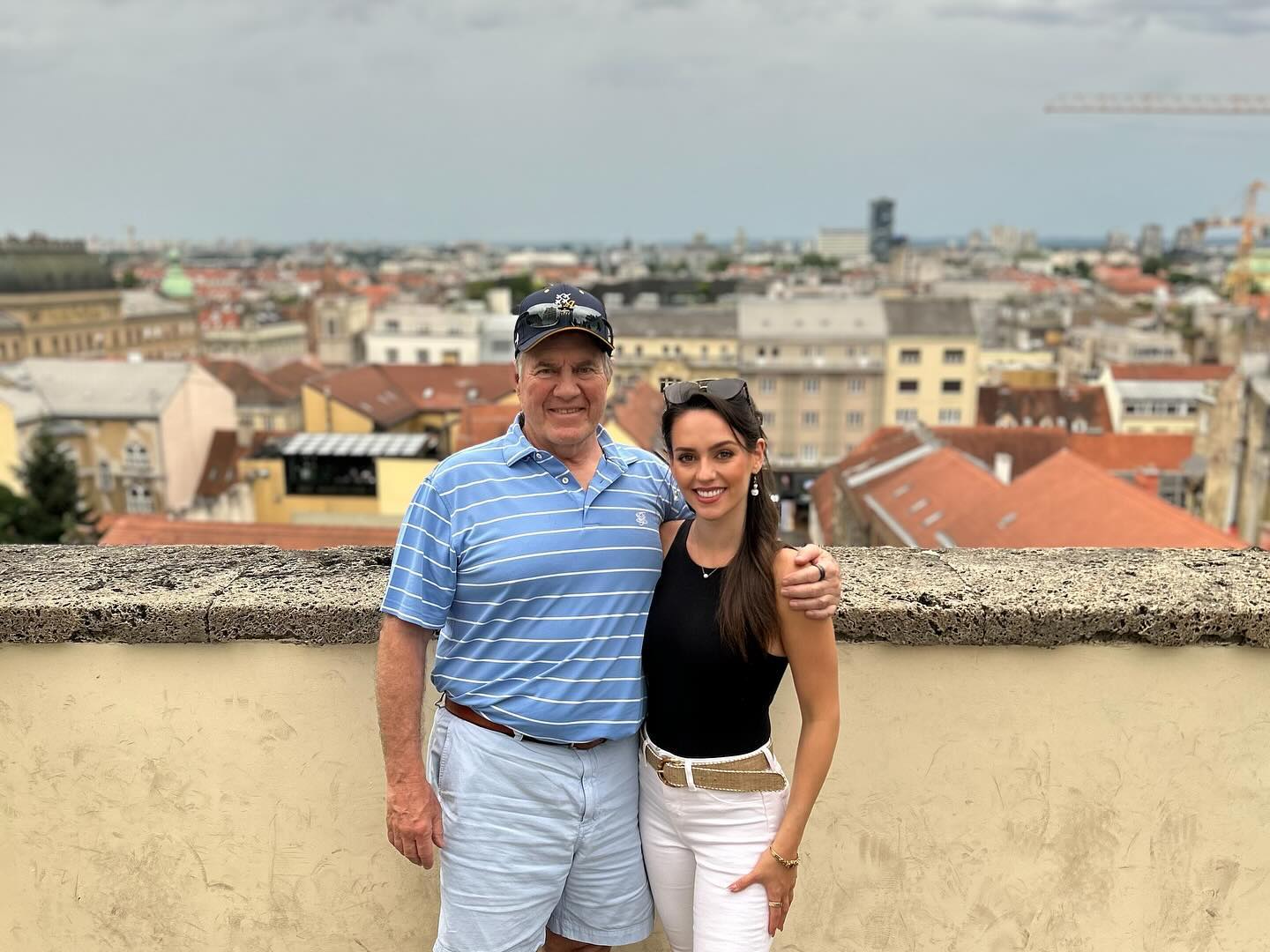 Jordon Hudson and Bill Belichick smiling with a city skyline in the background.