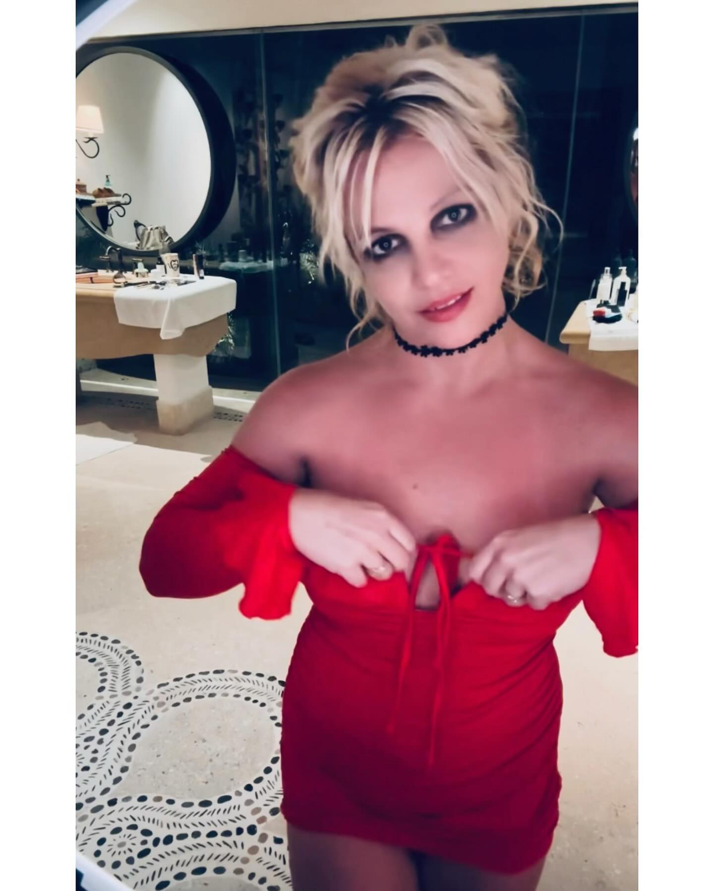 Britney Spears posing in a red off-the-shoulder dress and a black choker necklace.
