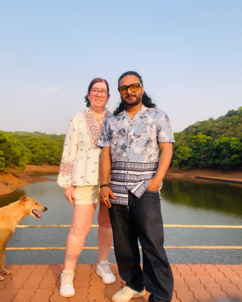 Jenny Slatten and Sumit, from "90 Day Fiancé", stand on a bridge with a dog, a lake, and trees in the background.