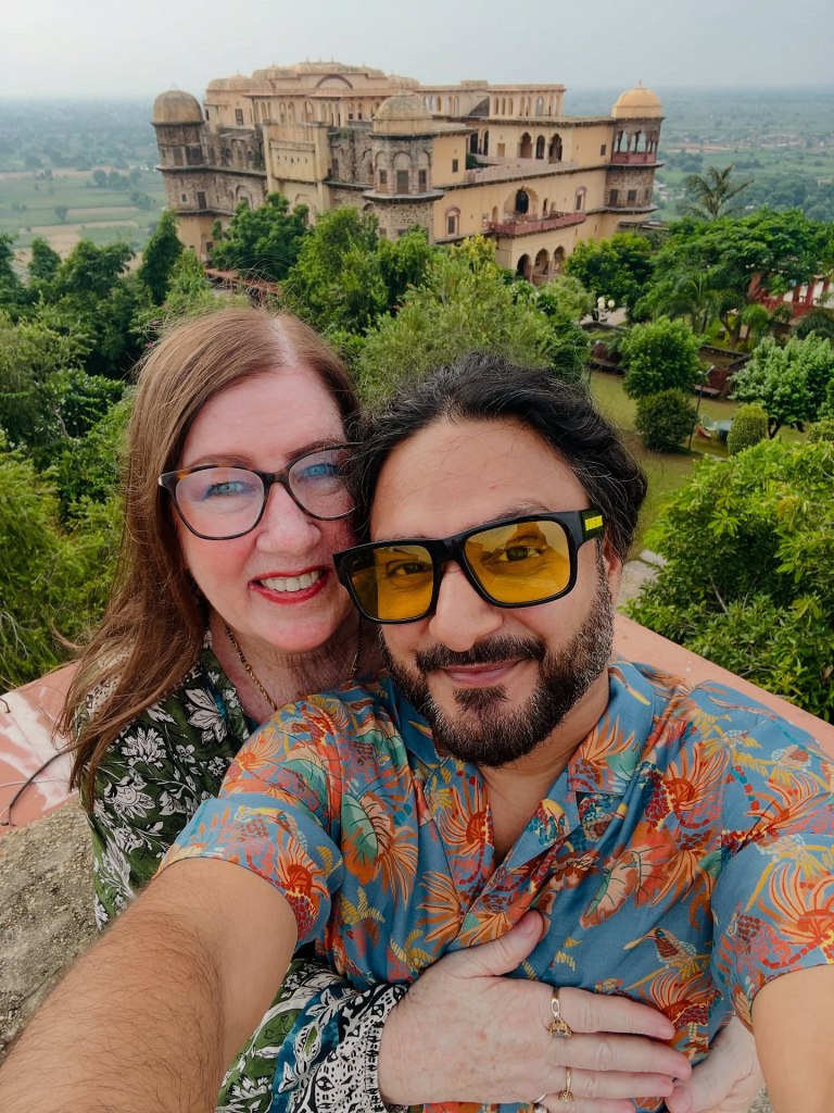 Jenny Slatten and Sumit pose for a selfie with a historic building and green landscape in the background.