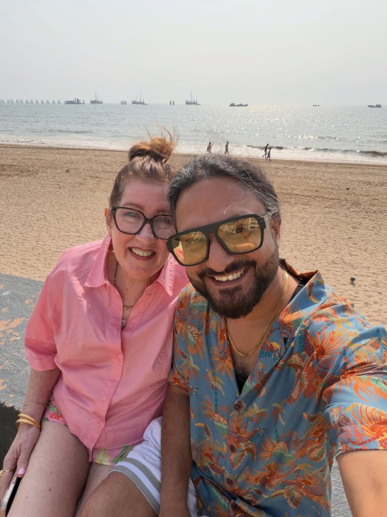 Jenny Slatten and Sumit Singh smiling for a selfie at a beach.