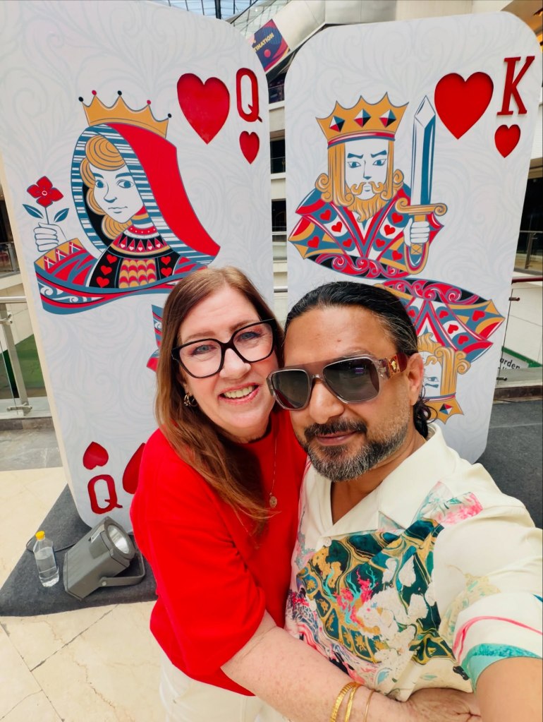 Jenny Slatten and Sumit Singh smiling in front of large Queen of Hearts and King of Hearts playing cards.