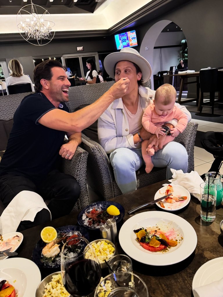 Scott McGillivray feeding Brooke Hogan's husband, who is holding a baby, at a restaurant.