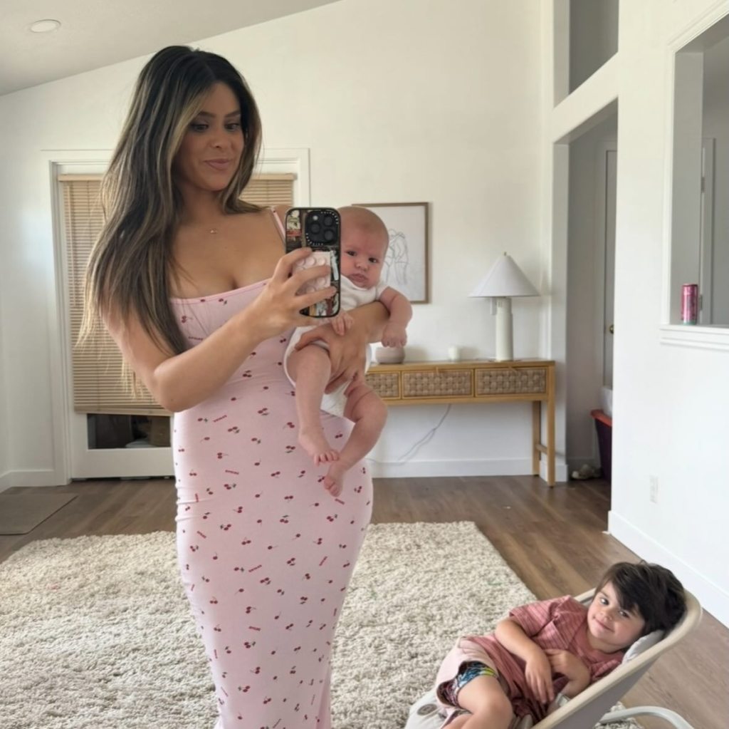 Taylor Frankie Paul taking a mirror selfie holding her baby, with her other child lounging in a bouncer on the floor.