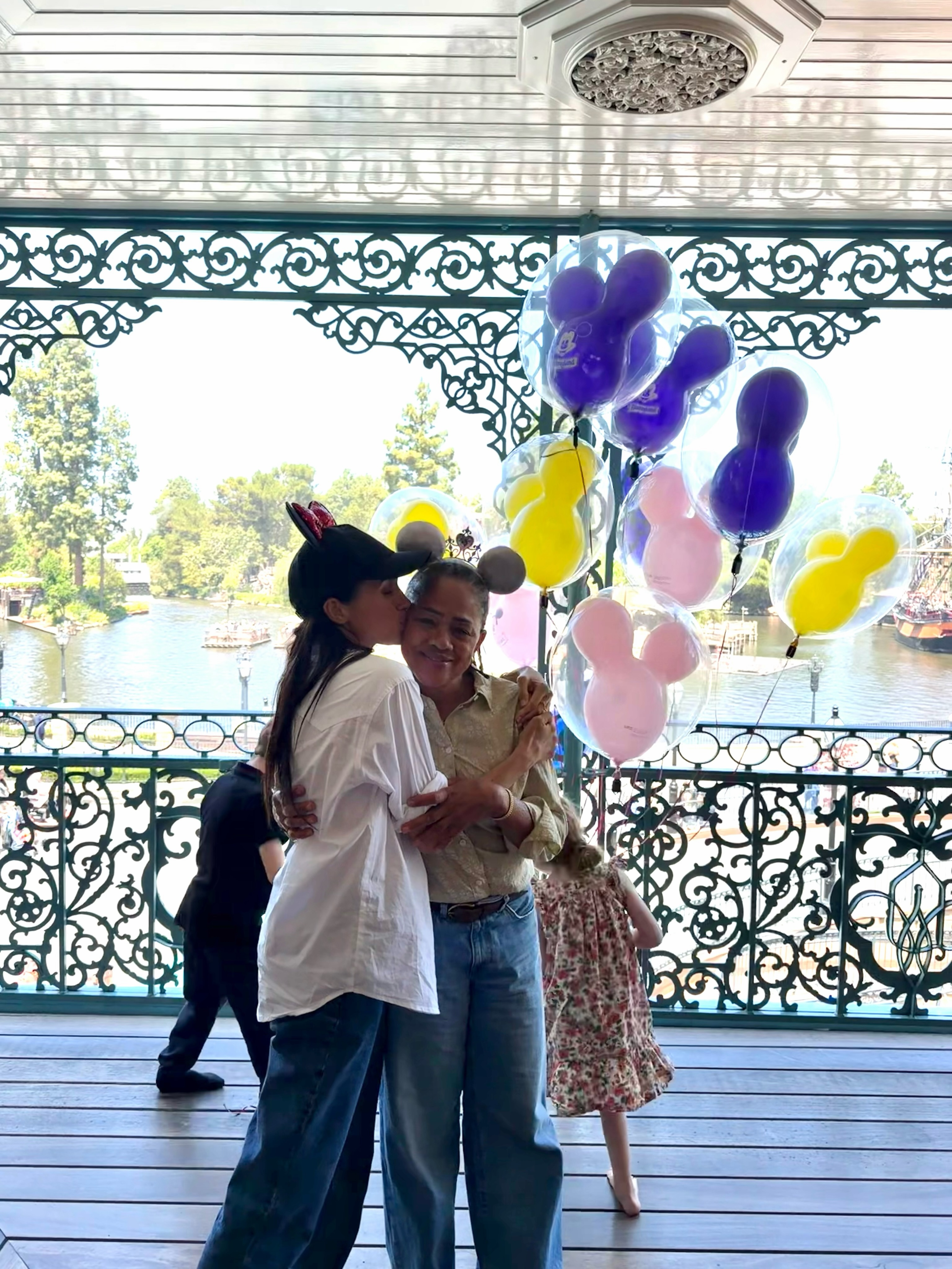 Meghan Markle kisses her mother, Doria Ragland, while holding Mickey Mouse balloons at Disneyland.