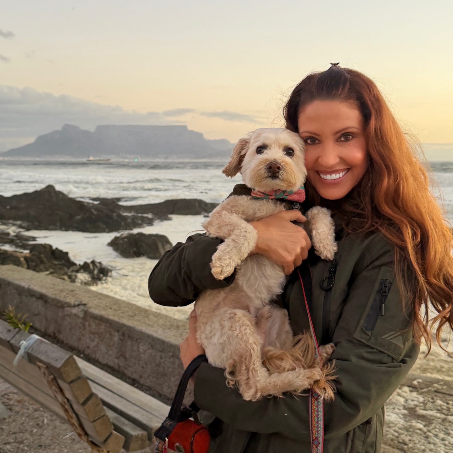 Shannon Elizabeth holding her dog with a mountain and ocean in the background.