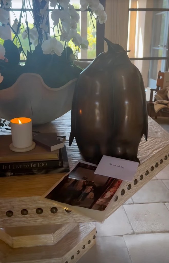 A bronze penguin sculpture next to a lit candle, a book, a photograph, and a card that reads "The one and only."