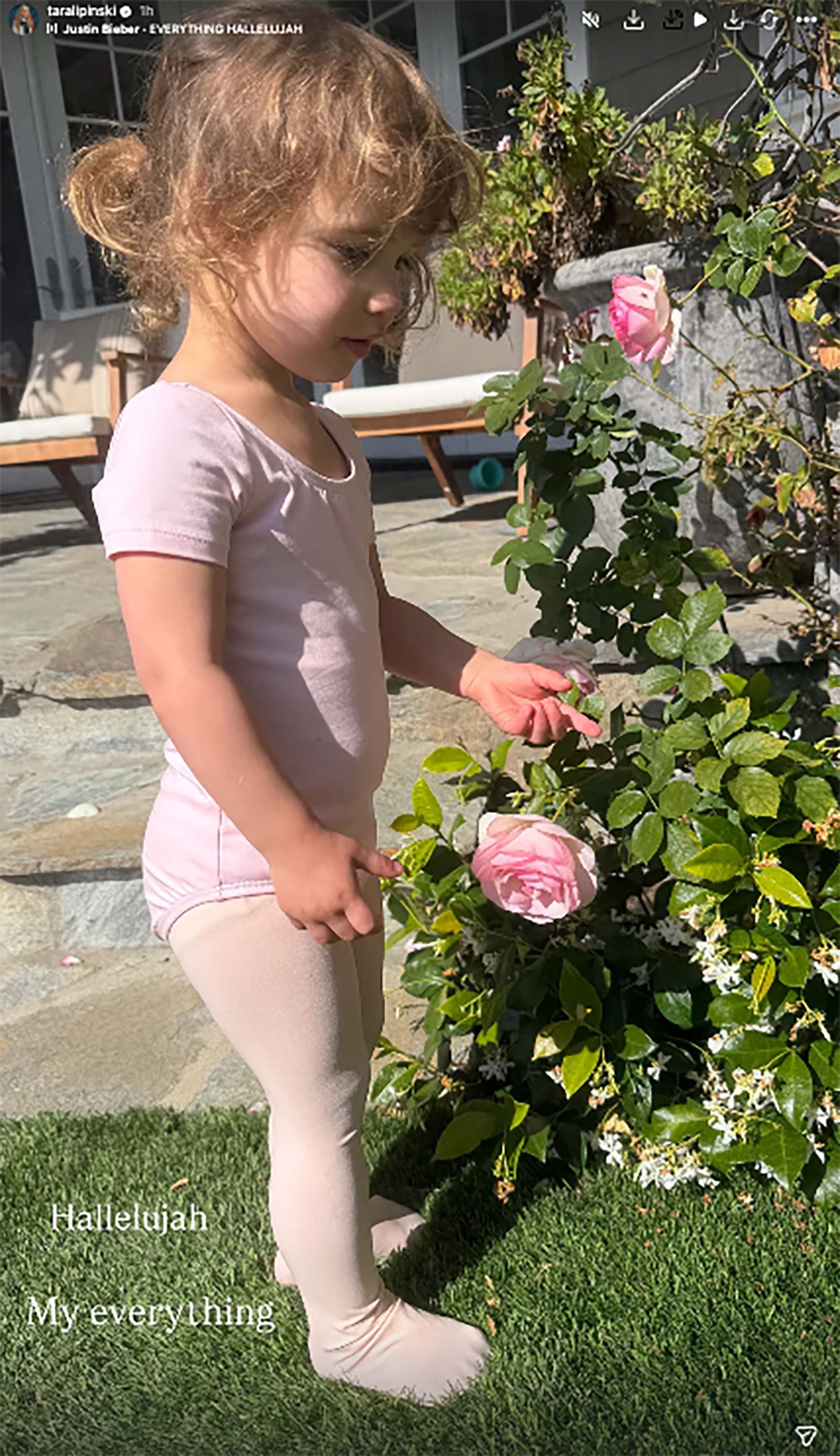 Tara Lipinski's daughter in a pink leotard and tights touching a pink rose.
