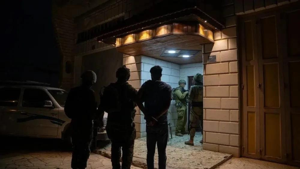 Israeli soldiers and an arrested suspect standing outside a building at night.