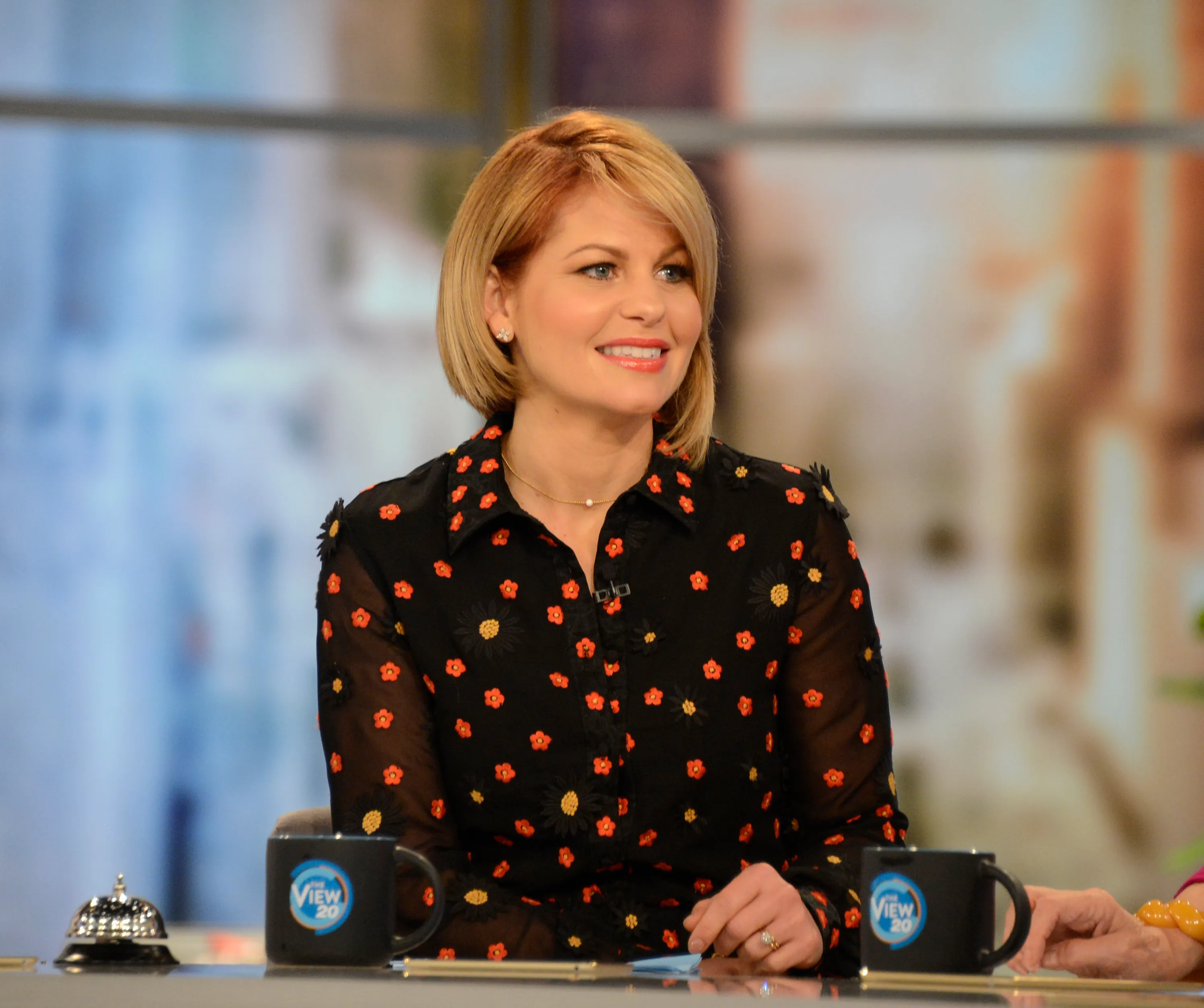 Candace Cameron Bure on the set of "The View" with two mugs featuring "The View 20" logo in the foreground.