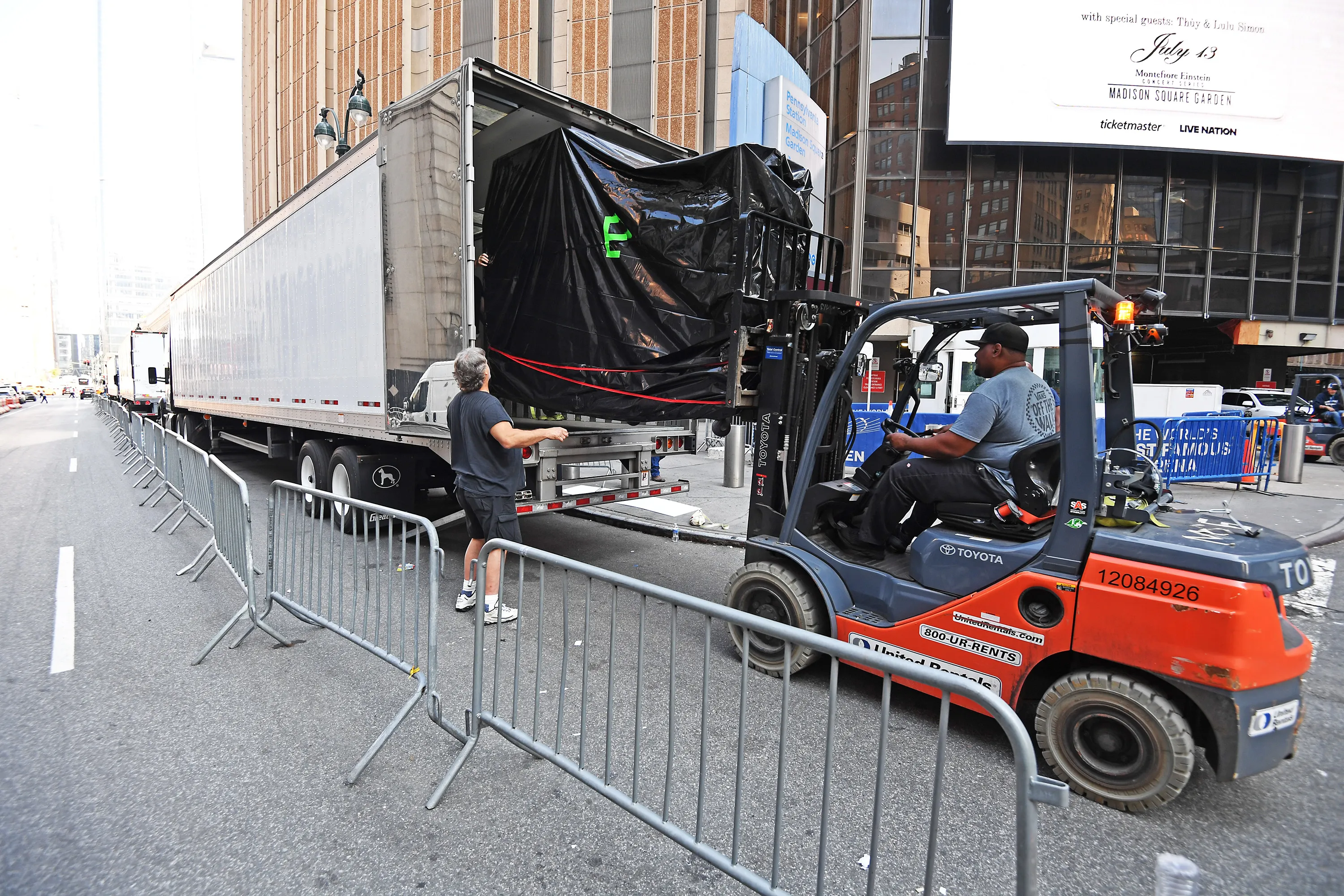 A forklift moves a large, black, covered object from an 18-wheeler truck at Madison Square Garden's loading dock.