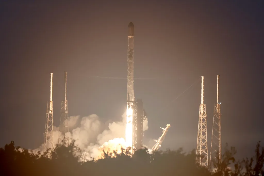 SpaceX Falcon 9 rocket lifting off with bright orange exhaust against a dark sky.
