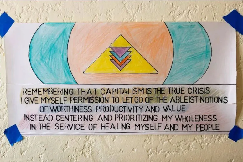A hand-drawn sign taped to a wall reads, "Remembering that capitalism is the true crisis I give myself permission to let go of the ableist notions of worthiness productivity and value instead centering and prioritizing my wholeness in the service of healing myself and my people."