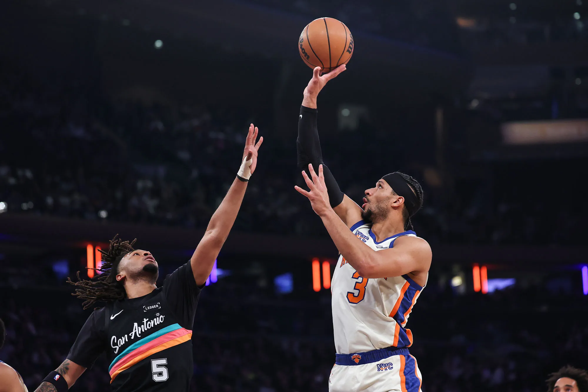 Basketball player in white and orange jersey shoots over opponent in black jersey.