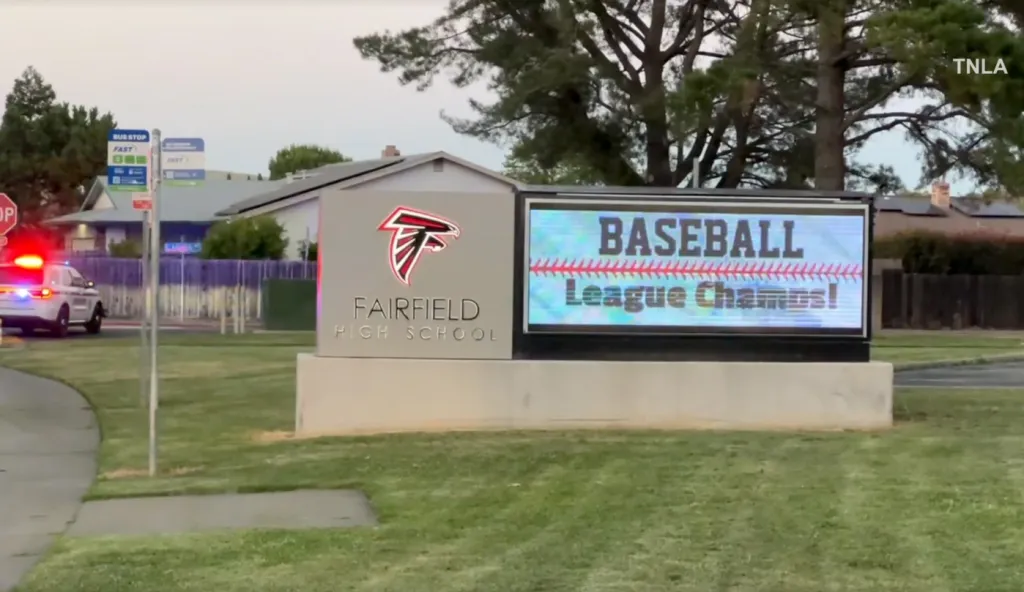 Fairfield High School sign with a digital display showing "BASEBALL League Champs!" and a police car with flashing lights in the background.