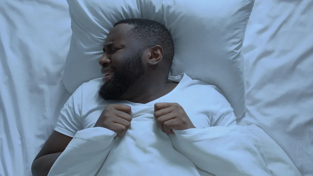 A top-down view of an anxious man waking up from a nightmare in a bed with white sheets and pillow.
