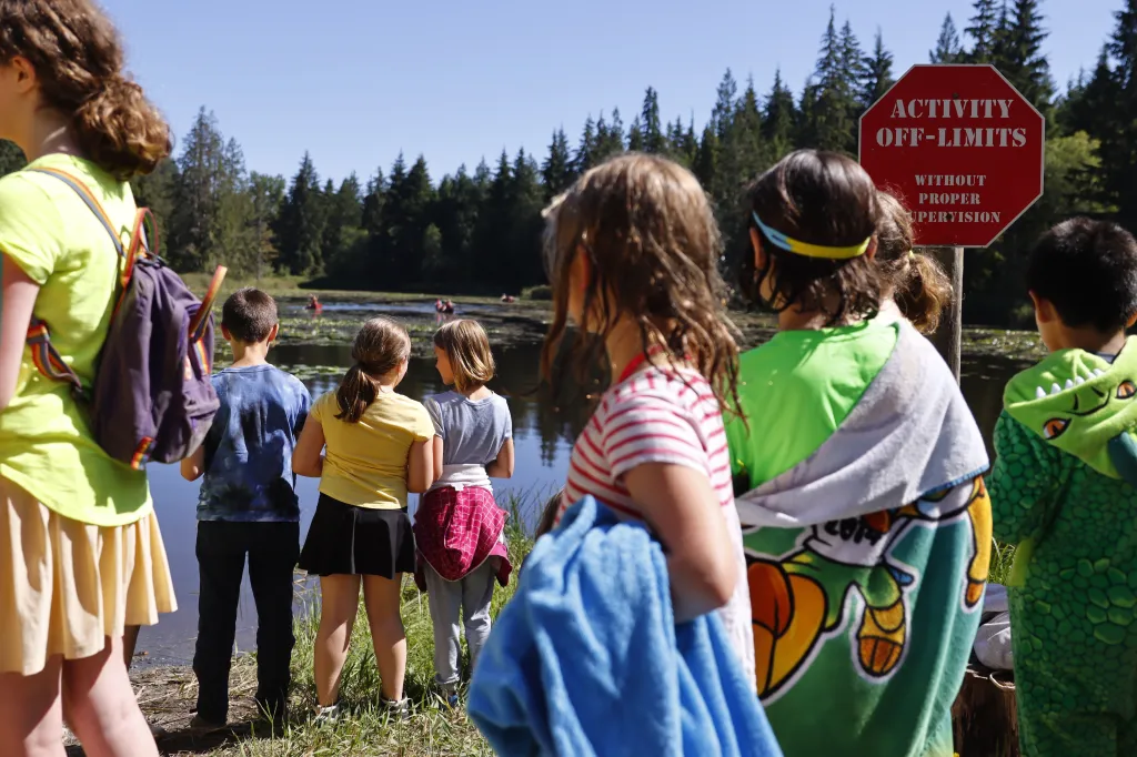 Campers at a Jewish summer camp look out at a lake with several people in canoes, with a red "Activity Off-Limits" sign visible.