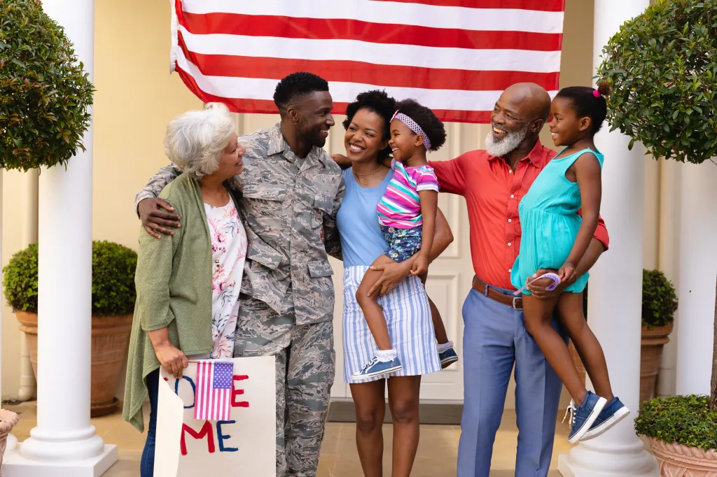 A cheerful African American family with a soldier and a "Welcome Home" sign, with an American flag in the background.