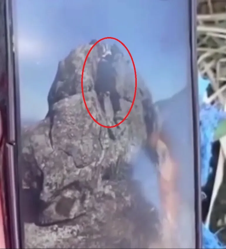 Video grab of a hiker falling from a towering rock viewpoint, highlighted by a red circle.