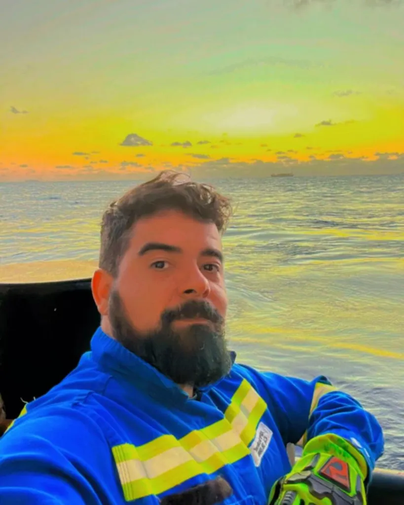 Caio Rocha Aguiar Arrabal posing for a photo with a body of water and a sunset in the background.