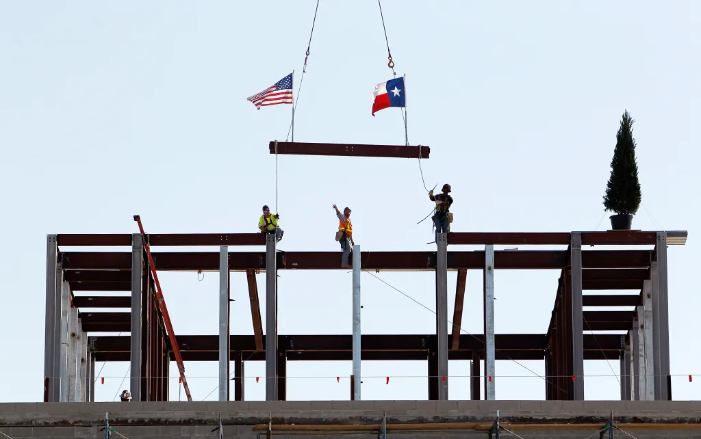 Three ironworkers guide the final steel beam into place on the George W. Bush Presidential Center.