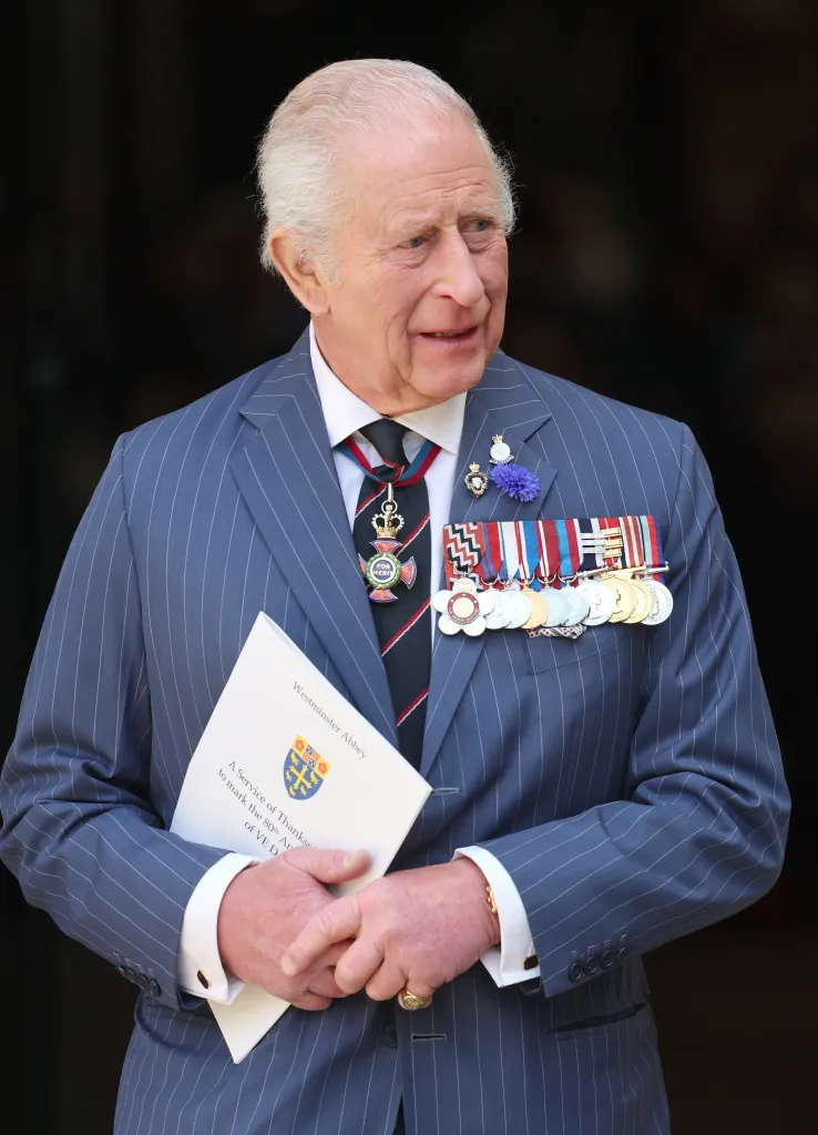 King Charles III in a pinstriped suit, with military medals pinned to his chest, holds a program for the VE Day 80th-anniversary service.