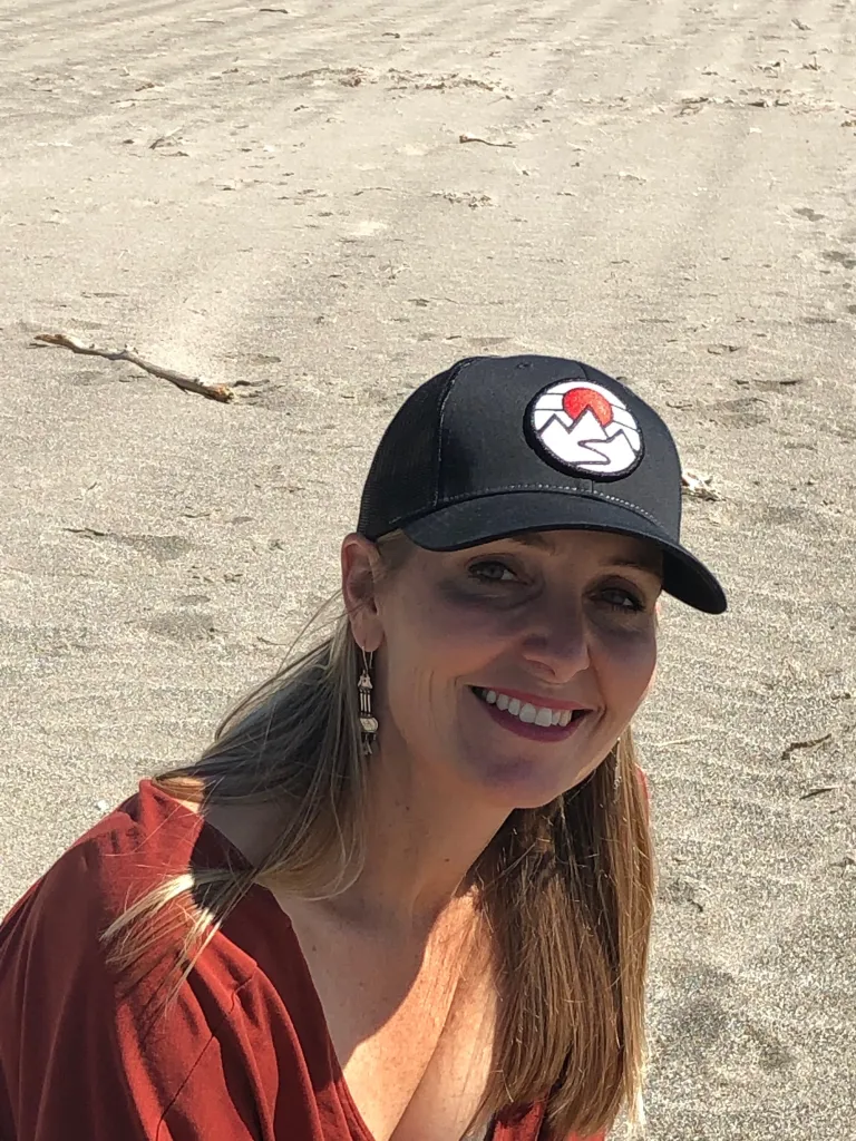 A woman wearing a black cap with a mountain and sun logo, smiling at the camera.